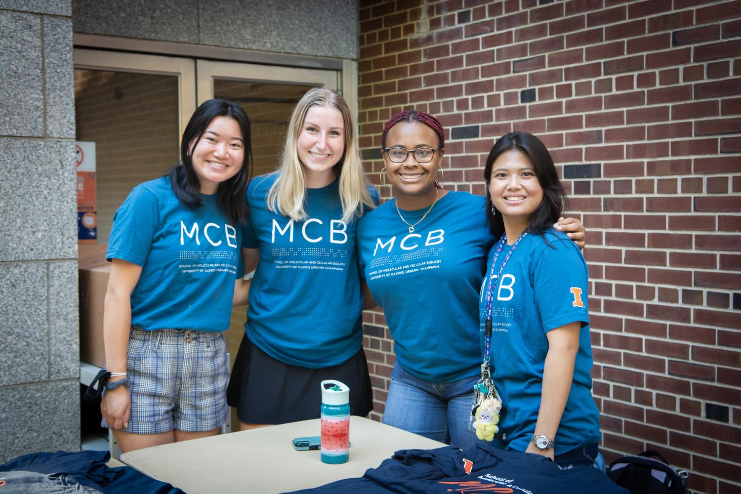 Four MCB students put arms around each other while greeting new students at a welcome back picnic.